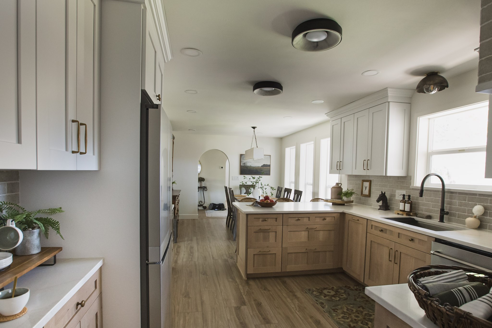 The kitchen looking through to the dining room, with an oak island, black flush-mount lights, and a long table beyond